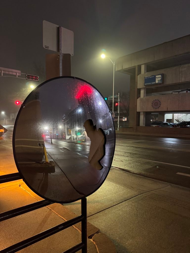 A shattered parking garage mirror set against a nighttime streetscape